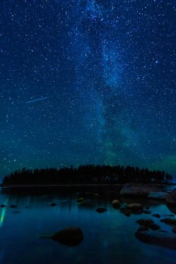 Taşlar ve ormanlarla dolu deniz suyunun üzerinde yıldızlı bir gökyüzü olan gece manzarası. Birçok yıldız, Samanyolu ve takımyıldızlı Astrofotoğrafçılık