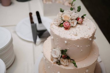 Masada gül çiçekleriyle süslenmiş beyaz düğün pastası.