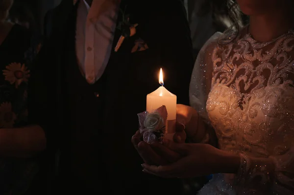 hands of the bride and groom hold a lighted candle on the wedding day during the ceremony