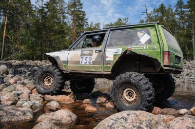 KARELİYA, RUSSIA REUKLİK - CIRCA HAZİRAN, 2022: Ladoga Gölü çevresindeki off-road turnuvası Ladoga Kupası 2022. 4x4 SUV yazın doğada bir off-road yarışında kayaların üzerinden geçer.