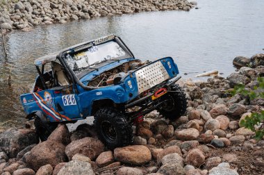 KARELİYA, RUSSIA REUKLİK - CIRCA HAZİRAN, 2022: Ladoga Gölü çevresindeki off-road turnuvası Ladoga Kupası 2022. UAZ 4x4 arazi aracı, doğadaki bir gölde kayaların üzerinde bir yarışta yol alır.