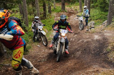 KARELİYA, RUSSIA REÜKLİK - CIRCA HAZİRAN 2022: Karelia 'da Ladoga Kupası 2022 off-road turnuvası. Enduro spor motosikletli motosikletçiler bir motokros yarışında ormanda kayalık bir tepeye tırmanırlar.