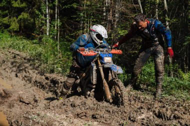 KARELİYA, RUSSIA REÜKLİK - CIRCA HAZİRAN 2022: Karelia 'da Ladoga Kupası 2022 off-road turnuvası. Kirli motosiklet yarışçıları, motokros yarışmasında Forest Road 'da çamurdan bir spor motosikleti çıkarıyorlar.