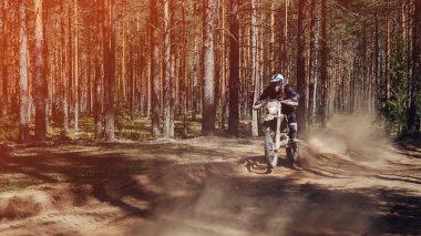 Dayanıklı bir spor motosiklet yarışçısı güneşli bir günde, ormanın tozlu yollarında hızlı gider.