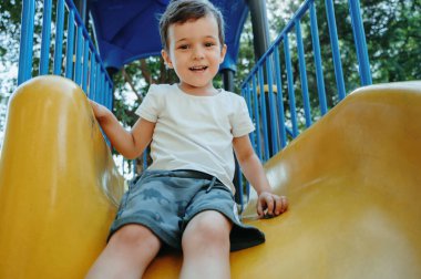 Mutlu çocuk yazın çocuk parkında kayar.