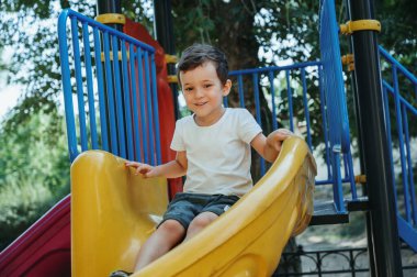 Mutlu çocuk yazın çocuk parkında kayar.