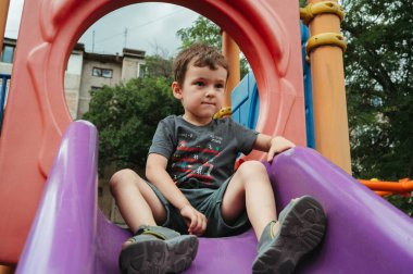 Anaokulu çocuğu yazın çocuk parkında bir slaytta oynar.