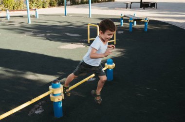 Anaokulu çocuğu yazın parktaki oyun parkında yatay barlarda oynar.