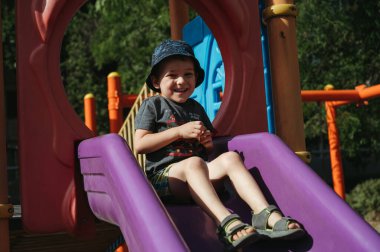 Mutlu anaokulu çocuğu yazın çocuk parkında kayıyor.