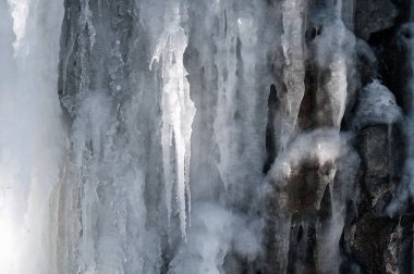 Donmuş buz saçakları ve kışın taş bir duvarın üzerindeki krema.