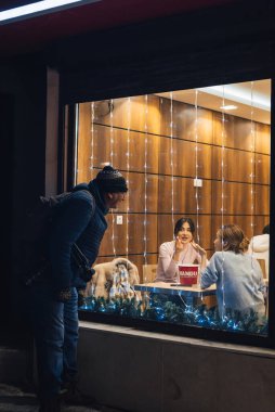 SHYMKENT, KAZAKHSAN - 23 HAZİRAN 2023: Evsiz adam geceleri bir kafenin penceresinde dilenir