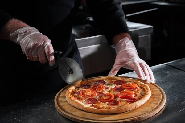chef cuts traditional Italian pepperoni pizza into slices with a knife in the kitchen