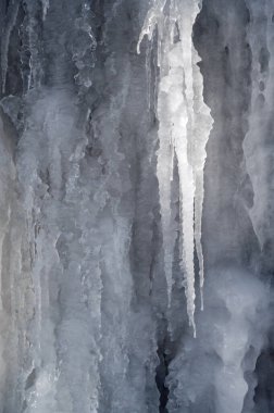 Donmuş buz saçakları ve kışın taş bir duvarın üzerindeki krema.