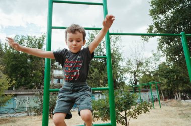 Anaokulu çocuğu yazın oyun parkındaki yatay barlardan atlıyor.