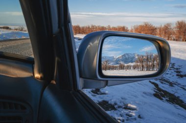 Tien Shan Dağları 'nın kış manzarasının yansıması ve arabanın dikiz aynasında karlı tarlalarda ağaçlar. Kazakistan 'da şenlikli kış yolculuğu kavramı