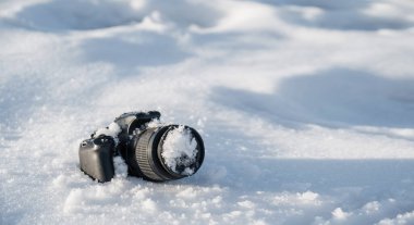 Donmuş lensli profesyonel dijital slr fotoğraf makinesi kışın bir kar yığınında fotokopi alanı ile birlikte yatıyor.