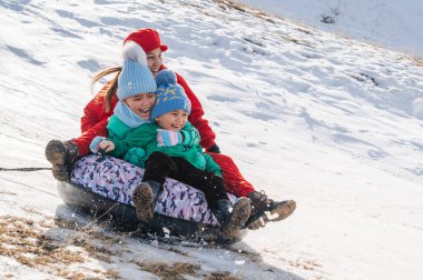 TAU SAMALY, KAZAKHSTAN - 23 Aralık 2023: Mutlu Kazak ailesi kışın Kazakistan 'daki Tau Samaly dinlenme merkezinde karla birlikte bir kaydırak kaydırağına iniyor.