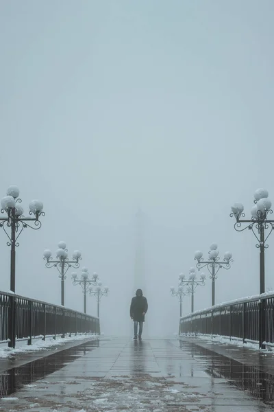 silhouette lonely man maniac walks on a foggy bridge with lanterns in winter with snow and fog mist