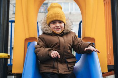 Mutlu çocuk kışın oyun parkında kaydırak oynuyor.