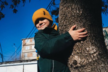 Küçük çocuk sonbaharda oyun parkında bir ağaca tırmanıyor.