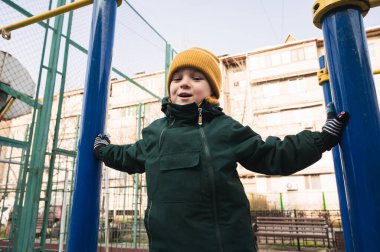 Mutlu çocuk sonbaharda parktaki oyun parkındaki yatay parmaklıklara tırmanıyor.