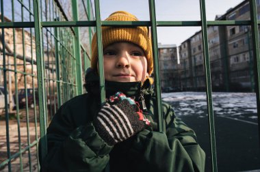 Sonbaharda bir çocuk parkında parmaklıklar arkasında yalnız bir çocuğun portresi.