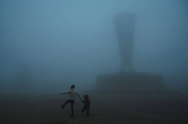 Akşamları sisli mistik bir parkta yürüyen çocuklu bir anne kadının sırtından. Sonbaharda, Kazakistan 'ın Şymkent kentindeki Independence Park' ta sisli bir sis bulutunda, insanların olduğu sisli bir manzara.
