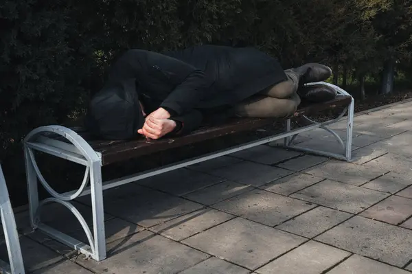 无家可归 心烦意乱的男人躺在公园的长椅上 图库照片