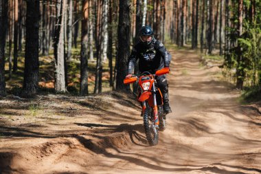KARELİYA, RUSSIA REÜKLİK - CIRCA HAZİRAN 2022: Karelia 'da Ladoga Kupası 2022 off-road turnuvası. Dayanıklı spor motosiklet yarışçısı ormandaki tozlu yolda motosiklet sürüyor. Motokros yarışında.