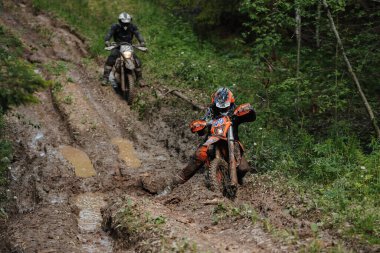 KARELİYA, RUSSIA REÜKLİK - CIRCA HAZİRAN 2022: Karelia 'da Ladoga Kupası 2022 off-road turnuvası. Enduro spor motosikletli motosiklet yarışçıları orman yolundaki çamurlu su birikintilerinde geziyorlar.