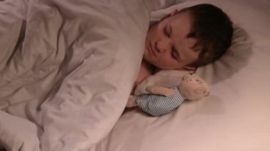 Küçük çocuk gece yatakta oyuncak ayıya sarılarak huzursuzca uyuyor. Oğlu kâbus görüyor.