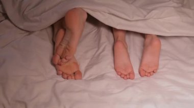 Oğlu ve annesinin huzursuz ayakları gece çarşafta battaniyenin altında kaşınıyor ve kadın bacakları uyuştu. Anne kadın ve kız çocuk yatakta kaşınmaktan çıplak ayakla tırmalanıyor.