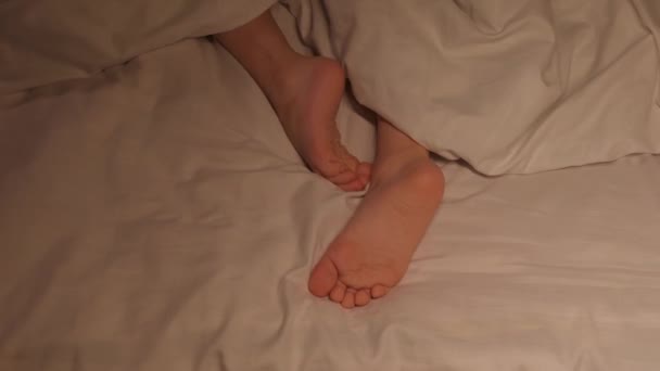 夜に毛布の下のシートに 子供の足が落ち着かない 裸足のベビーガールは 夜のベッドルームで寝ることはありません — ストック動画