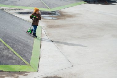 Anaokulu öğrencisi çocuk sonbaharda kaykay rampasında parkta scooter sürüyor.