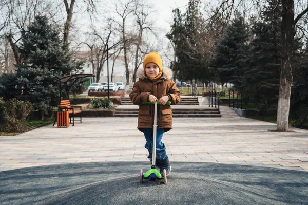 Anaokulu öğrencisi çocuk sonbaharda parkta scooter kullanıyor.