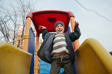Mutlu gülümseyen çocuk sonbaharda çocuk parkında kayıyor.