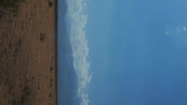 Kazakistan 'ın bozkırlarında Tien Shan dağlarıyla bir yaz günü manzarası. Otobanda hareket eden bir arabanın dikey yavaş çekim videosu.