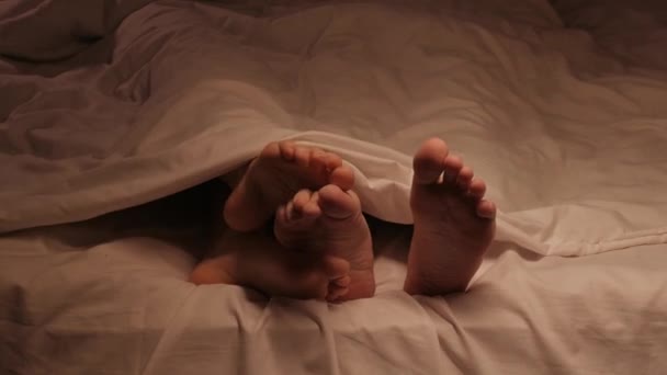 couple of male and female legs enjoy and touching other under a blanket on a sheet in the evening before sex and sleeping. Foreplay and love between a man and a woman in bed in the bedroom