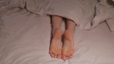 Kadın ayakları, beyaz bir çarşafta battaniyenin altında geceleri uykularında hareket eder. Bir kadın otel odasındaki bir yatakta çıplak ayakla uyuyor.