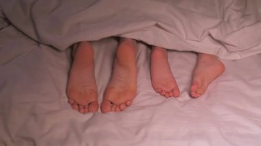 Erkek çocuk ve anne ayağının dans eden bacakları akşamları battaniyenin altında yatar. Mutlu kız bebek kız ve kadın anne yatak odasında çıplak ayakla oynaşıyor.