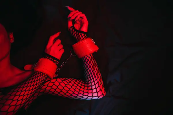 female hands in leather BDSM handcuffs. Submissive woman slave girl is lying on the bed. Hardcore sex with submission, domination, punishment and violence