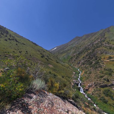Yazın vadideki bir tarlada çağlayan şelalelerle dolu bir dağ nehri. Gökyüzü görünümü üstü