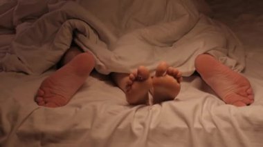 Bir çiftin bacakları, bir otel odasındaki beyaz bir çarşafın üzerinde battaniyenin altında seks yapıyor. Bir erkek ve bir kadın sevişiyor.