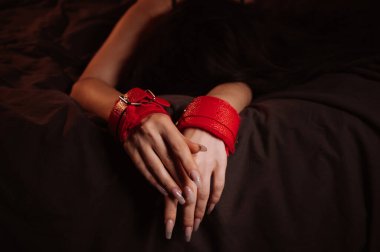 Deri kelepçeli kadın elleri teslim olmak ve siyah bir çarşaf üzerinde hakimiyet seksi yapmak için yakın plan. İtaatkar kadın köle kız yatak odasında yatıyordu.