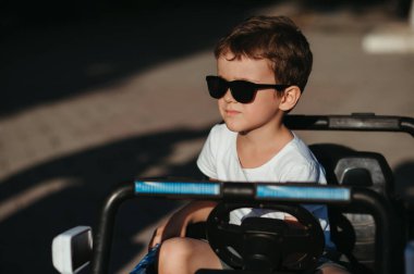 Yazın parkta oyuncak bir arabada güneş gözlüklü bir çocuğun portresi.