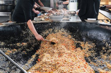 Erkek şefler, restoranın mutfağında büyük bir kazanda sebzeli Özbek pirinç pilavı pişiriyor. Orta Asya Pilaf Merkezi Besh Qozon, Özbekistan, Taşkent