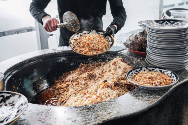 Erkek aşçı, mutfakta büyük bir kazandan pişirilmiş Özbek pilavını bir tabağa koyar. Geleneksel Doğu Arap mutfağı pirinç ve kuzu etiyle