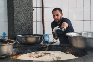Erkek, Orta Asya Pilaf Merkezi Besh Qozon 'daki bir kazanda geleneksel Özbek pilavı için kimyon ile pirinç pişiriyor. Taşkent, Özbekistan - 16 Nisan 2024