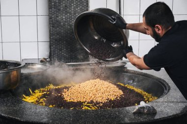 Erkek aşçı, Orta Asya Pilaf Merkezi Besh Qozon 'da Özbek pilavı pişirmek için havuç ve nohutlu bir kazana böğürtlen ekliyor. Taşkent, Özbekistan - 16 Nisan 2024