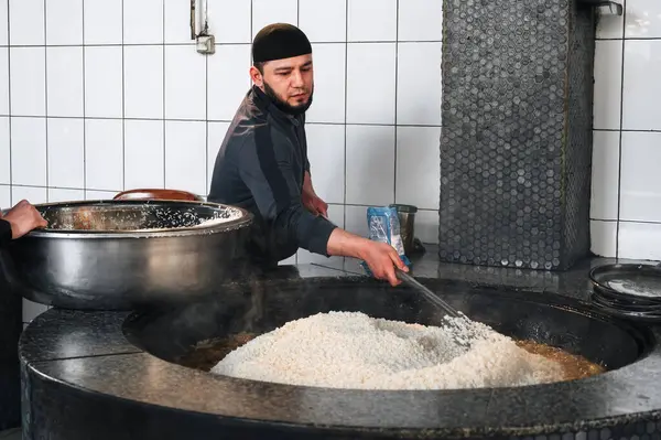 Erkek aşçı, Orta Asya Pilaf Merkezi Besh Qozon 'da geleneksel Özbek pilavını pişirmek için bir kazanda pirinç karıştırıyor. Taşkent, Özbekistan - 16 Nisan 2024